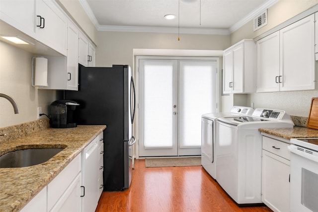 clothes washing area with sink, washer and clothes dryer, ornamental molding, and light hardwood / wood-style floors