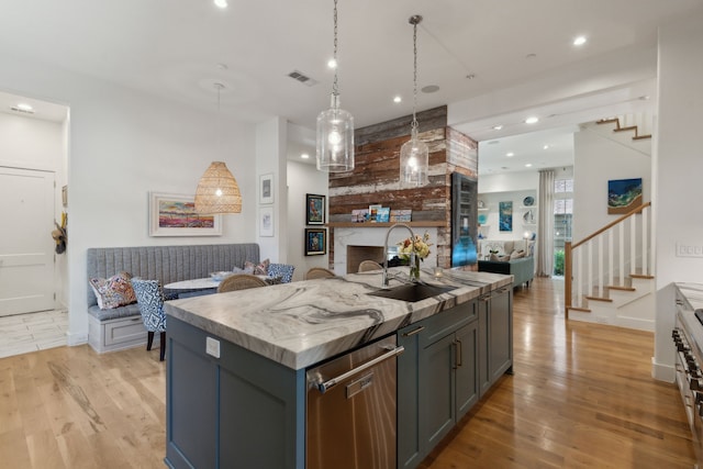 kitchen with an island with sink, sink, hanging light fixtures, stainless steel dishwasher, and light hardwood / wood-style flooring