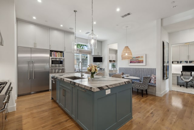 kitchen featuring sink, white cabinetry, hanging light fixtures, built in appliances, and a center island with sink