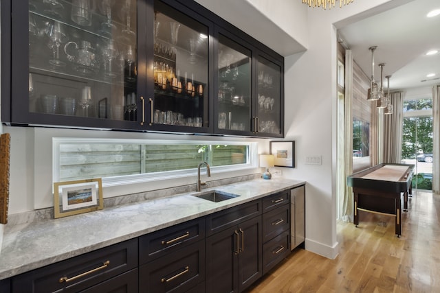 bar with sink, pendant lighting, light stone counters, and light wood-type flooring