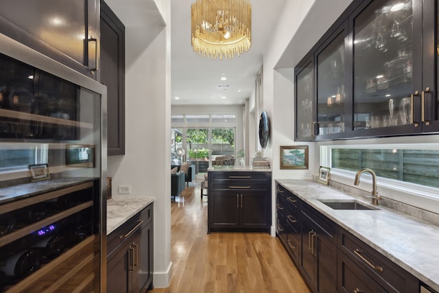 bar featuring sink, an inviting chandelier, light stone counters, light hardwood / wood-style floors, and decorative light fixtures