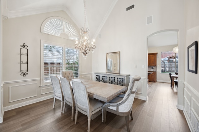 dining area with dark wood-type flooring, crown molding, a chandelier, and high vaulted ceiling