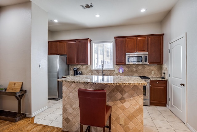 kitchen with a kitchen breakfast bar, stainless steel appliances, a center island, and light tile patterned flooring