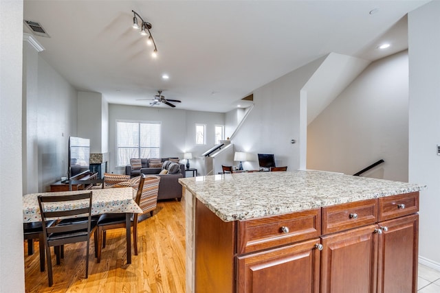 kitchen featuring a kitchen island, light stone counters, ceiling fan, track lighting, and light hardwood / wood-style flooring