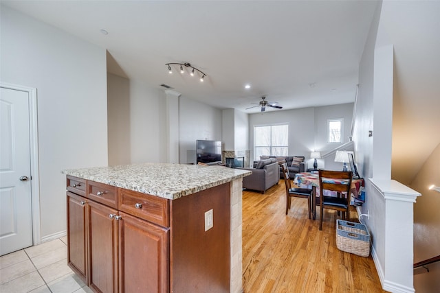 kitchen with light stone countertops, a center island, ceiling fan, and light wood-type flooring