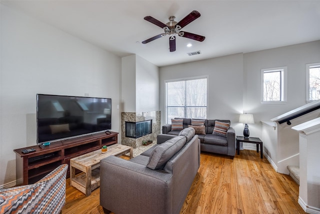 living room with a fireplace, a wealth of natural light, ceiling fan, and light wood-type flooring