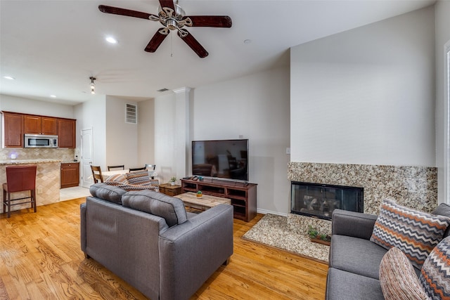 living room with a premium fireplace, ceiling fan, and light hardwood / wood-style flooring