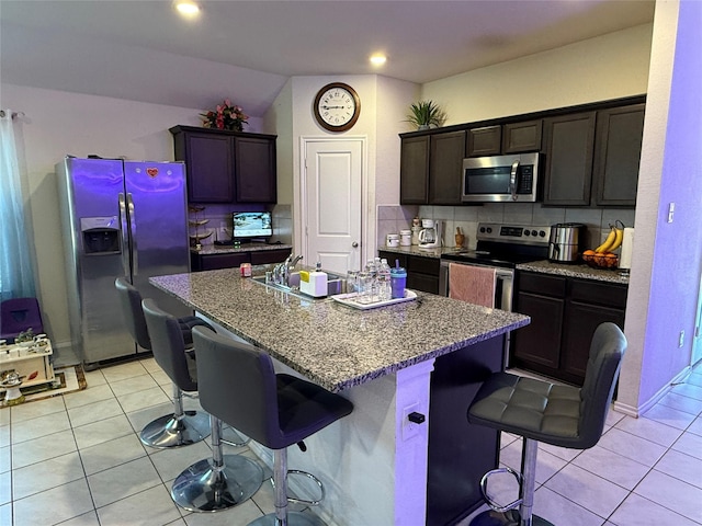 kitchen with dark brown cabinetry, a kitchen bar, a center island with sink, and appliances with stainless steel finishes