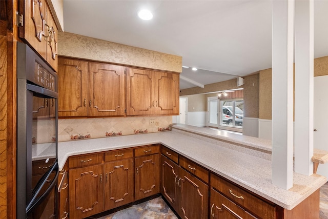 kitchen featuring light stone counters, double oven, decorative backsplash, and kitchen peninsula