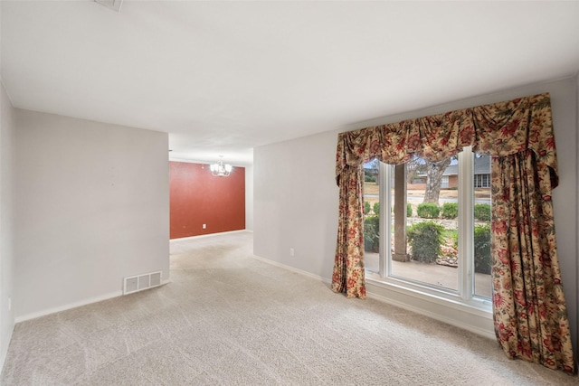 spare room featuring light carpet and a chandelier