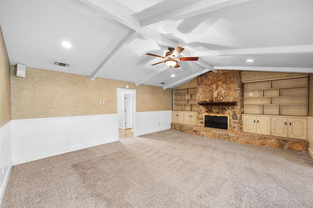 unfurnished living room with built in shelves, a stone fireplace, vaulted ceiling with beams, ceiling fan, and carpet