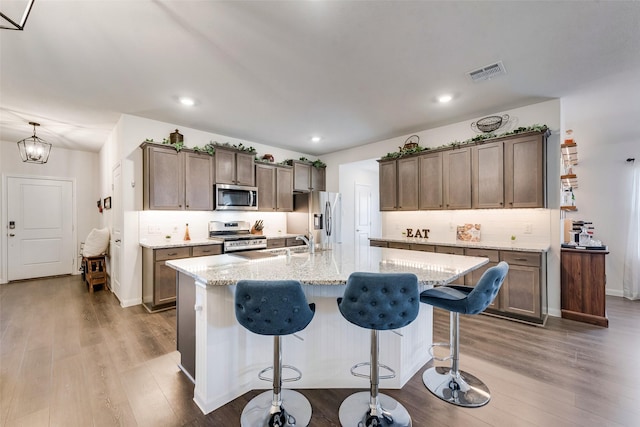 kitchen with visible vents, hanging light fixtures, a kitchen island with sink, and stainless steel appliances