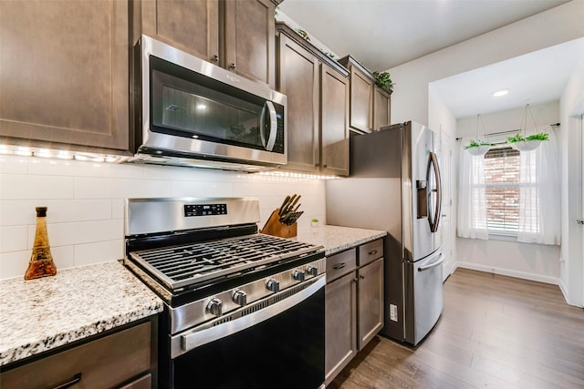 kitchen with tasteful backsplash, appliances with stainless steel finishes, dark wood-type flooring, dark brown cabinets, and light stone countertops