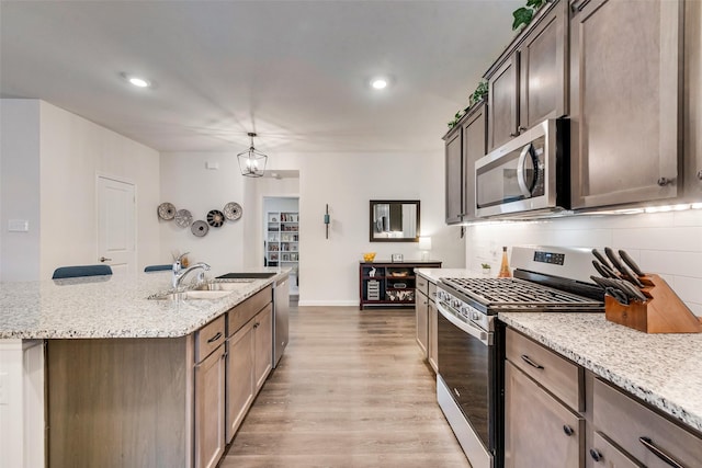 kitchen with a center island with sink, decorative backsplash, appliances with stainless steel finishes, light wood-style floors, and a sink