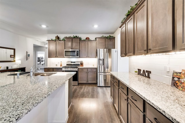 kitchen featuring stainless steel appliances, backsplash, dark wood-type flooring, a sink, and light stone countertops