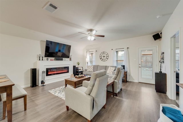 living area with ceiling fan, visible vents, wood finished floors, and a glass covered fireplace