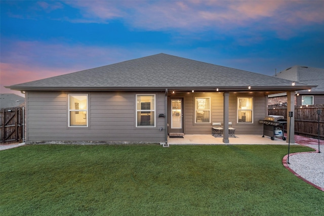 back of property at dusk featuring a shingled roof, a yard, and fence