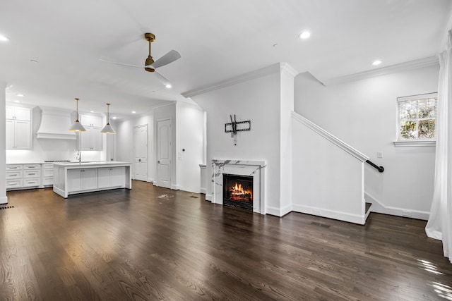 unfurnished living room with crown molding, ceiling fan, a high end fireplace, and dark wood-type flooring