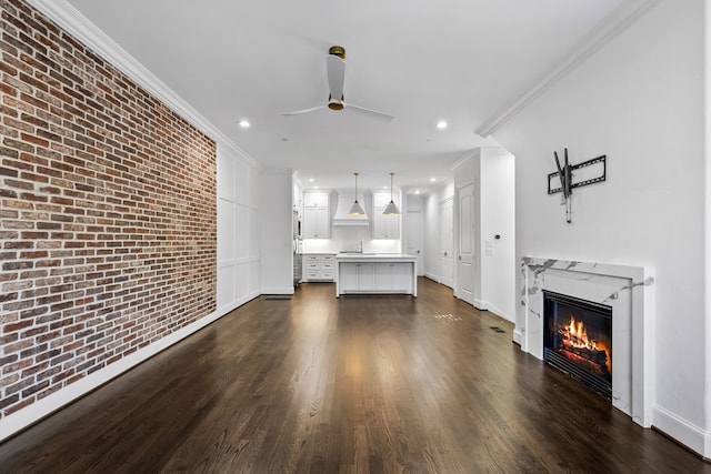 unfurnished living room with brick wall, dark hardwood / wood-style floors, ornamental molding, ceiling fan, and a premium fireplace