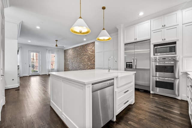 kitchen with sink, built in appliances, decorative light fixtures, an island with sink, and white cabinets