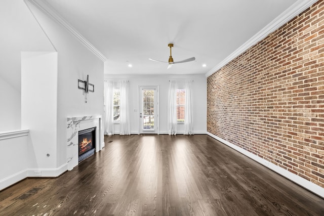 unfurnished living room with crown molding, ceiling fan, a fireplace, brick wall, and dark hardwood / wood-style flooring