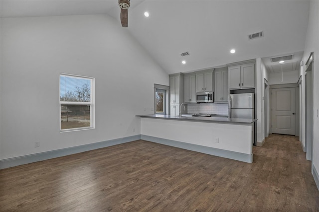 kitchen featuring dark wood-type flooring, appliances with stainless steel finishes, gray cabinets, kitchen peninsula, and decorative backsplash