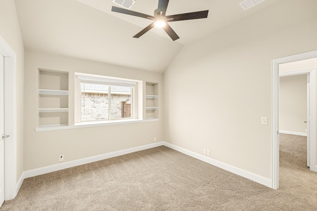 empty room featuring lofted ceiling, built in shelves, carpet floors, a ceiling fan, and baseboards