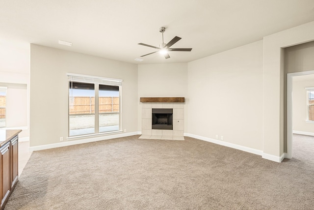 unfurnished living room featuring ceiling fan, a tile fireplace, baseboards, and light colored carpet