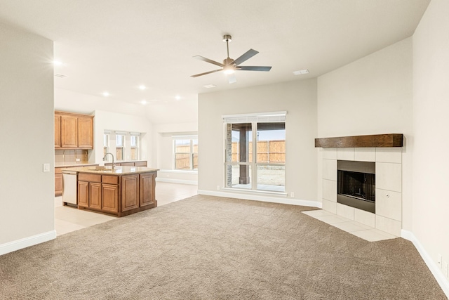 unfurnished living room with a tile fireplace, light colored carpet, a sink, and baseboards