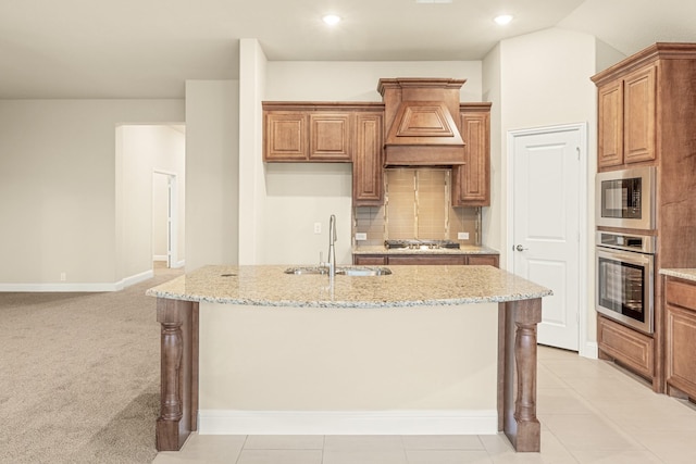 kitchen featuring a center island with sink, decorative backsplash, custom range hood, appliances with stainless steel finishes, and a sink