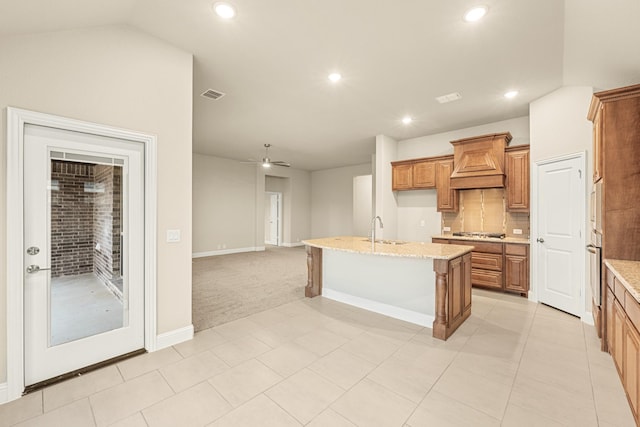 kitchen featuring visible vents, brown cabinetry, stainless steel appliances, premium range hood, and a sink