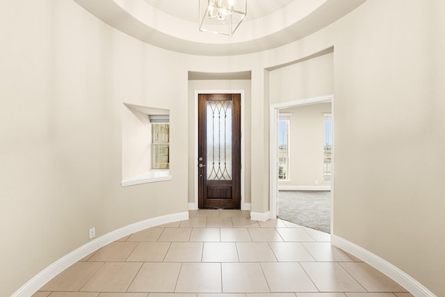 foyer featuring light tile patterned floors, a high ceiling, baseboards, a tray ceiling, and an inviting chandelier