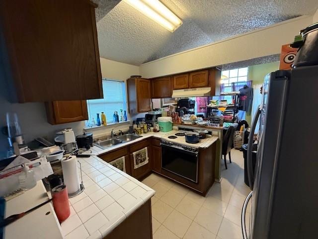 kitchen with stainless steel fridge, electric range oven, a textured ceiling, tile countertops, and kitchen peninsula