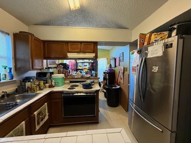 kitchen with sink, stainless steel fridge, electric range oven, a textured ceiling, and light tile patterned flooring