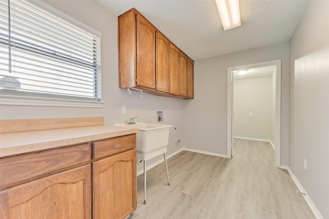 clothes washing area featuring cabinets, hookup for a washing machine, a textured ceiling, and light hardwood / wood-style flooring