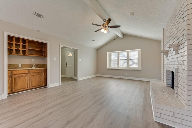 unfurnished living room with a brick fireplace, sink, a textured ceiling, and light wood-type flooring