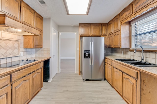 kitchen with stainless steel refrigerator with ice dispenser, premium range hood, sink, black electric stovetop, and light hardwood / wood-style floors