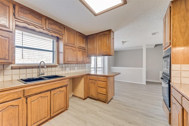 kitchen with sink, tasteful backsplash, light hardwood / wood-style floors, a textured ceiling, and oven