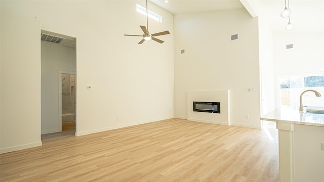 unfurnished living room featuring a towering ceiling, sink, light hardwood / wood-style flooring, and a wealth of natural light