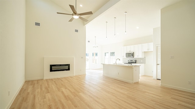 unfurnished living room with ceiling fan, a towering ceiling, sink, and light wood-type flooring