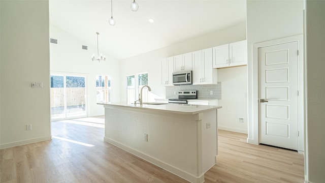 kitchen with sink, white cabinetry, hanging light fixtures, stainless steel appliances, and a center island with sink