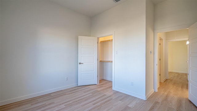 unfurnished bedroom with a towering ceiling, a closet, and light wood-type flooring