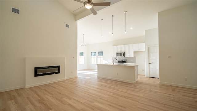 unfurnished living room with sink, high vaulted ceiling, ceiling fan, and light wood-type flooring