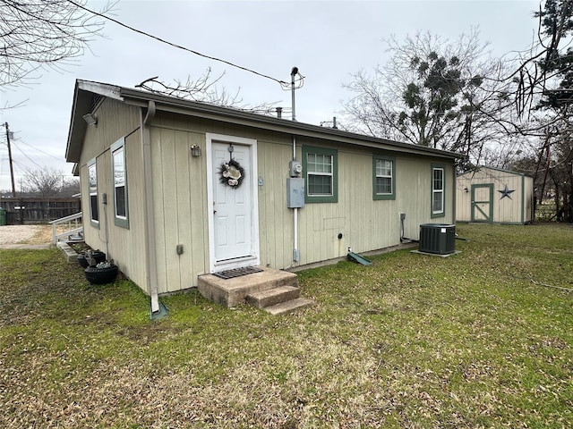 rear view of house with central AC unit, a lawn, and a storage unit