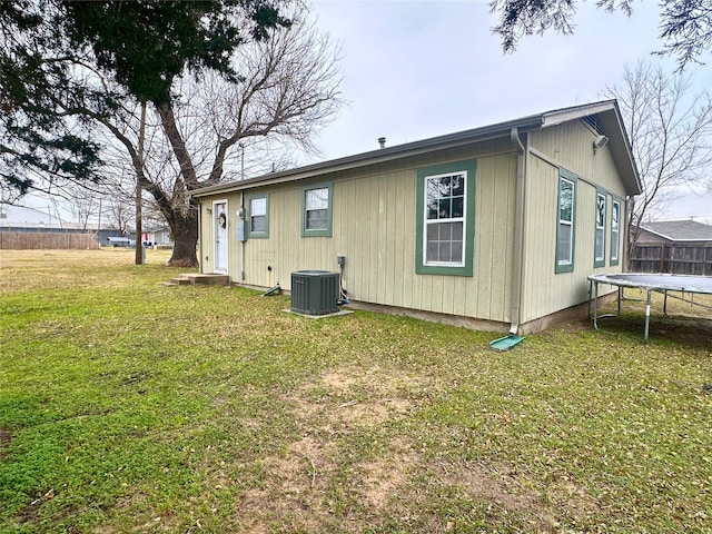 back of house featuring a trampoline, central AC unit, and a yard