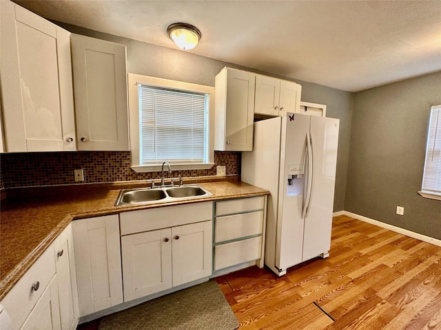 kitchen featuring sink, light hardwood / wood-style flooring, white fridge with ice dispenser, decorative backsplash, and white cabinets