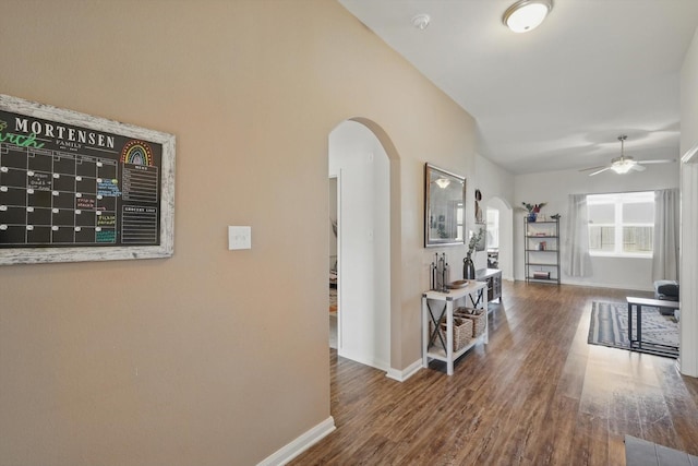 hall with baseboards, arched walkways, and wood finished floors