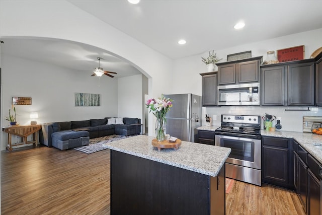 kitchen featuring light stone counters, arched walkways, stainless steel appliances, light wood-style flooring, and a kitchen island