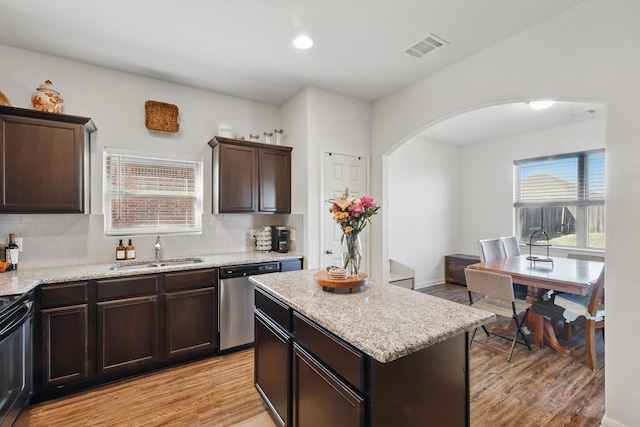 kitchen featuring arched walkways, visible vents, light wood-style floors, a sink, and dishwasher