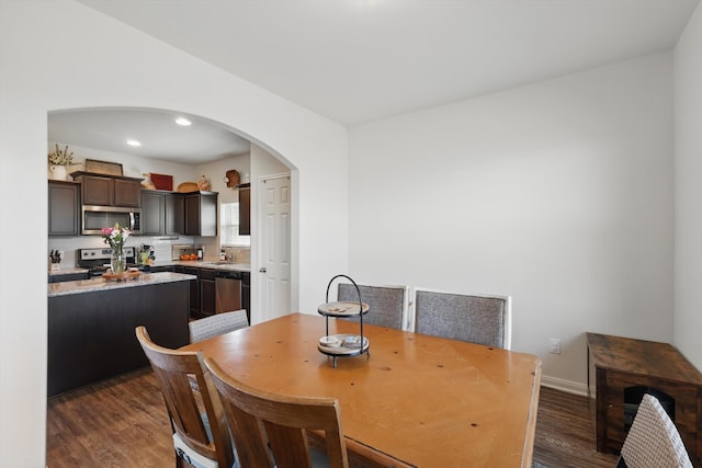 dining space with arched walkways, dark wood finished floors, baseboards, and recessed lighting